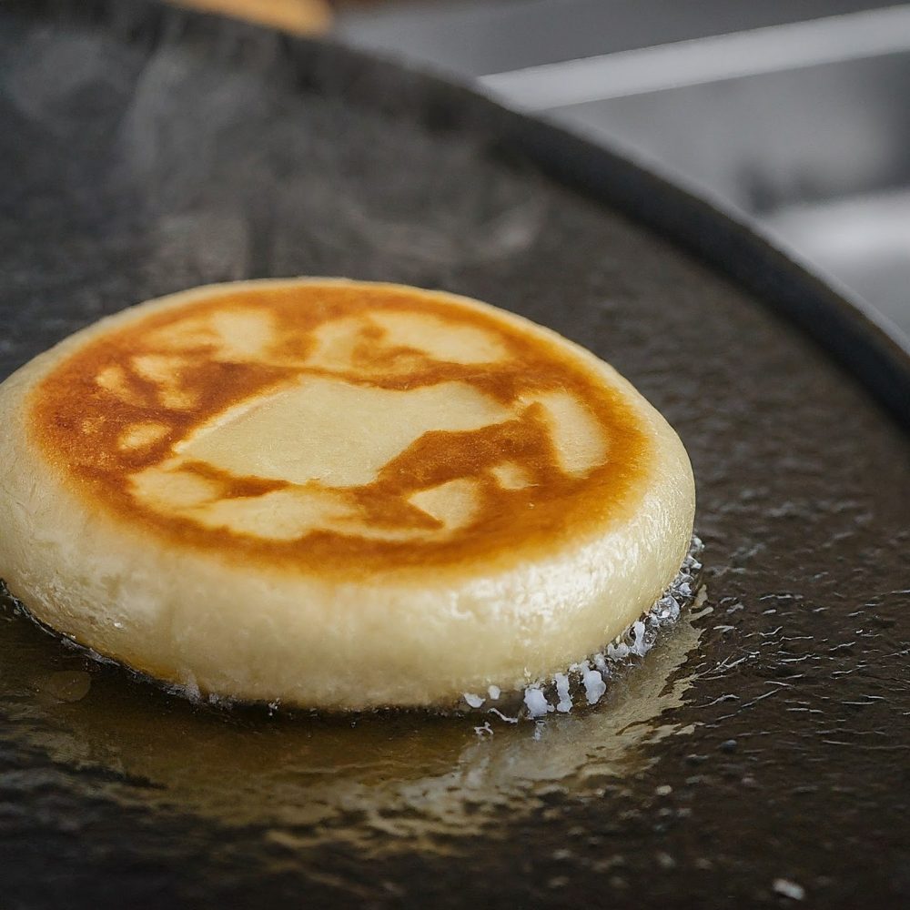 Image depicting A close-up of a sizzling bindaetteok being flipped on a griddle, showcasing its golden brown crust